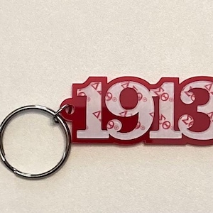 May include: Red plastic keychain with a white outline of the number 1913. The number is filled with a white pattern of the Greek letter Delta.