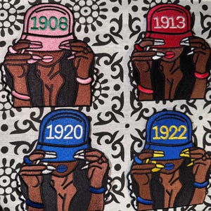 Peut inclure: Quatre écussons brodés représentant des personnages portant des casquettes de baseball avec les années 1908, 1913, 1920 et 1922. Chaque personnage a la peau foncée, de longs cheveux sombres et des mains près de la visière, avec des ongles manucurés.