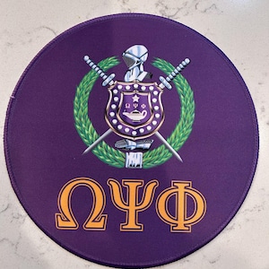 May include: A purple round patch with a gold Greek letter design that reads "ΩΨΦ". The center of the patch features a white knight with a sword and a shield with a purple lamp and a star.