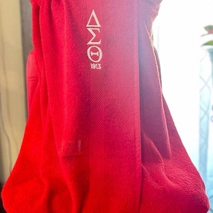 May include: A vibrant red towel with a white Greek letter design and the year 1913. The towel is wrapped around a form, showcasing its texture and color. The design is centered on the towel, adding a touch of elegance.