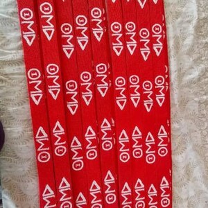 Puede incluir: Un conjunto de cordones rojos con texto blanco "OMD" y cierres met&aacute;licos. Los cordones est&aacute;n dispuestos verticalmente y apilados.