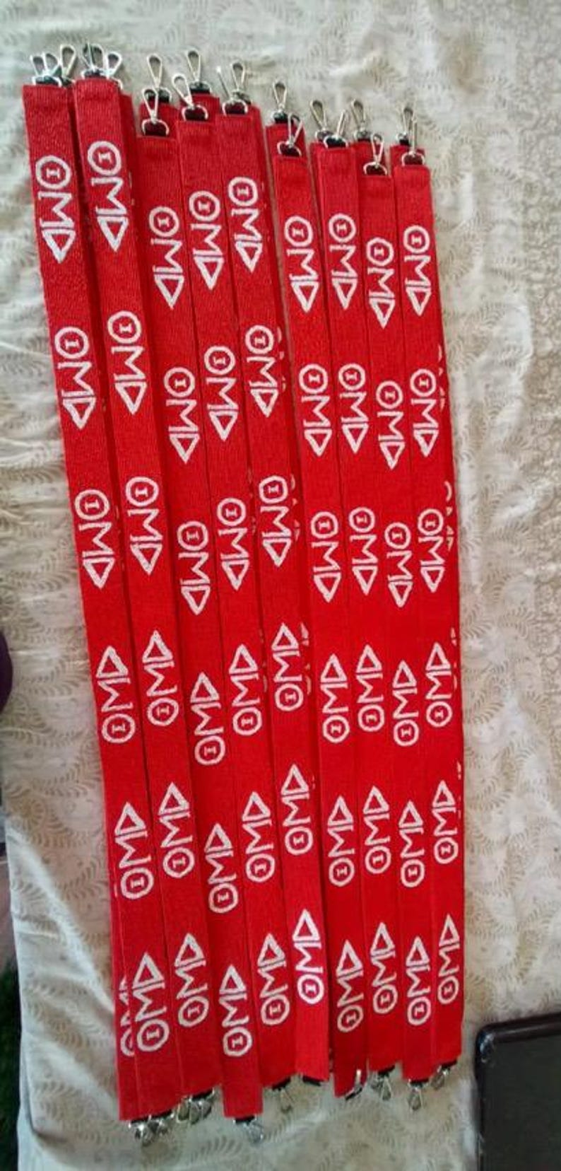 Puede incluir: Un conjunto de cordones rojos con texto blanco "OMD" y cierres met&aacute;licos. Los cordones est&aacute;n dispuestos verticalmente y apilados.