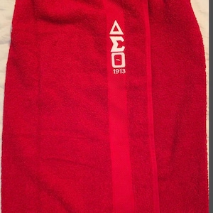 May include: A bright red towel wrap with a white Greek letter design and the number 1913. The towel has a soft, textured appearance and a vertical stripe down the center.