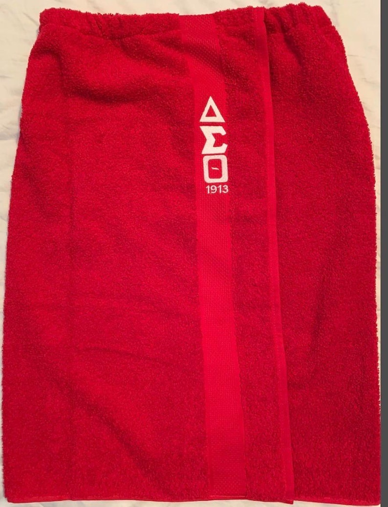 May include: A bright red towel wrap with a white Greek letter design and the number 1913. The towel has a soft, textured appearance and a vertical stripe down the center.