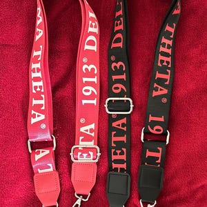 May include: Three adjustable bag straps in red and black, featuring white text that reads "MA THETA 1913 DELTA". Each strap has silver-colored metal hardware and a swivel clasp for attachment.