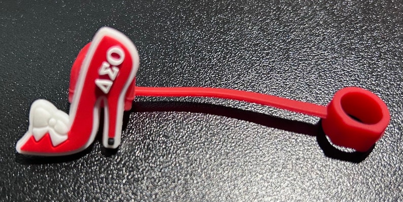 May include: Red high heel shoe charm with a white bow and the text "AZO" on the side. The charm is attached to a red silicone cord with a red silicone ring at the end.