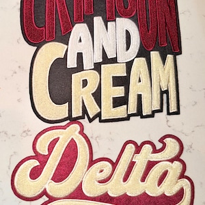 Peut inclure: Écussons brodés avec du texte rouge, blanc et crème. Le patch supérieur indique "CRIMSON AND CREAM" et le patch inférieur dit "Delta SIGMA THETA®". Les écussons sont sur une surface blanche.