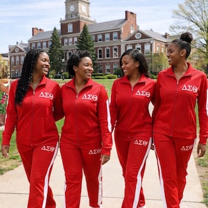 May include: Four people wearing matching red tracksuits with white accents and the Greek letters ΔΣΘ. The tracksuits include a zip-up jacket and pants. They are walking on a sidewalk in front of a brick building.