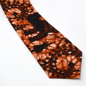 May include: A brown and black patterned tie with a design of stylized animals and plants. The tie is made of cotton fabric and has a pointed tip.