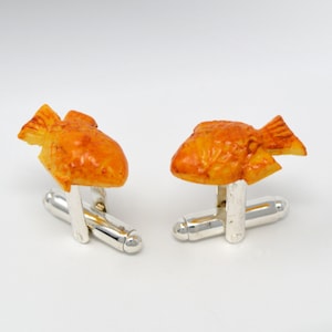 May include: A pair of silver cufflinks with a 3D design of a fried fish. The fish is orange and brown with a textured surface.