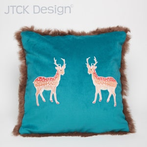May include: Teal velvet pillow with a brown faux fur trim featuring two embroidered deer in shades of orange and red. The pillow has the text "JTCK Design" in the top left corner.