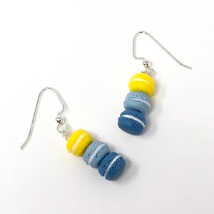 May include: A pair of silver dangle earrings with three stacked macarons. The macarons are blue and yellow with white frosting.