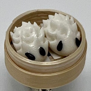 May include: Two white steamed buns with black sesame seeds in a bamboo steamer.