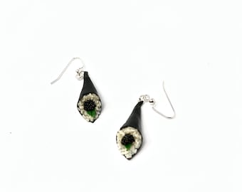 Puede incluir: Un par de pendientes de plata con forma de rollo de sushi negro y blanco con una hoja verde y caviar negro.