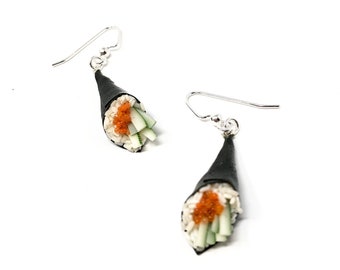 Puede incluir: Un par de pendientes de plata con forma de rollos de sushi. Cada pendiente tiene una envoltura de alga nori negra rellena de arroz blanco, huevas de pescado naranja y pepino verde.