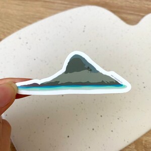 May include: A sticker featuring a green island with two palm trees and a blue ocean. The sticker has a white border and the text "HAY DESIGN CO." in the bottom right corner.
