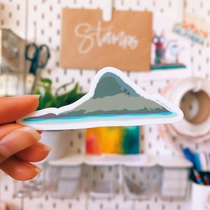 May include: A white sticker with a green and blue illustration of a small island with a mountain and palm trees. The sticker has the text "MAY DESIGN CO." in the bottom right corner.