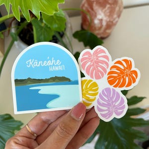 Four Monstera Leaves in purple, yellow, orange and pink. Monstera leaves are arranged in a pattern like a Hawaiian quilt design. Next to the Monstera Leaf sticker is an arched sticker with Kaneohe Bay, Hawaii illustrated.