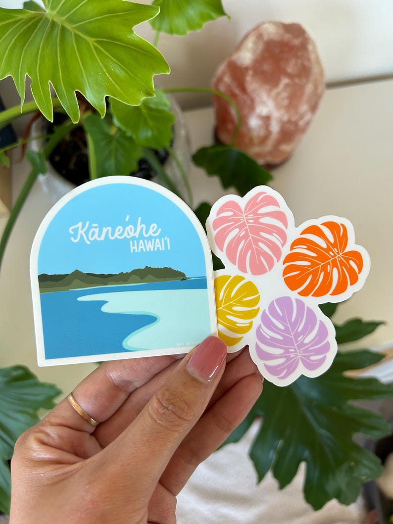Four Monstera Leaves in purple, yellow, orange and pink. Monstera leaves are arranged in a pattern like a Hawaiian quilt design. Next to the Monstera Leaf sticker is an arched sticker with Kaneohe Bay, Hawaii illustrated.