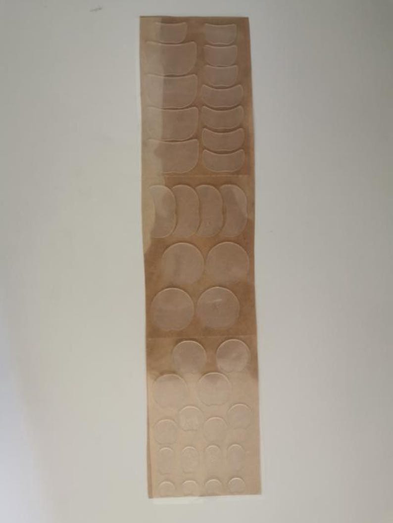 May include: A sheet of clear, adhesive, round and crescent-shaped eye patches on a brown paper backing.