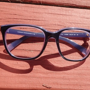 May include: Black and purple square-shaped eyeglasses with a blue frame. The text "REMARK! EXCHANGER 2 CE" is printed on the right arm of the glasses.