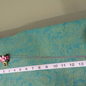 Peut inclure: Un collier avec pendentif Minnie Mouse et cha&icirc;ne argent&eacute;e. Le pendentif est color&eacute;, repr&eacute;sentant le visage et le n&oelig;ud de Minnie. Le collier mesure environ 35,5 cm de long.