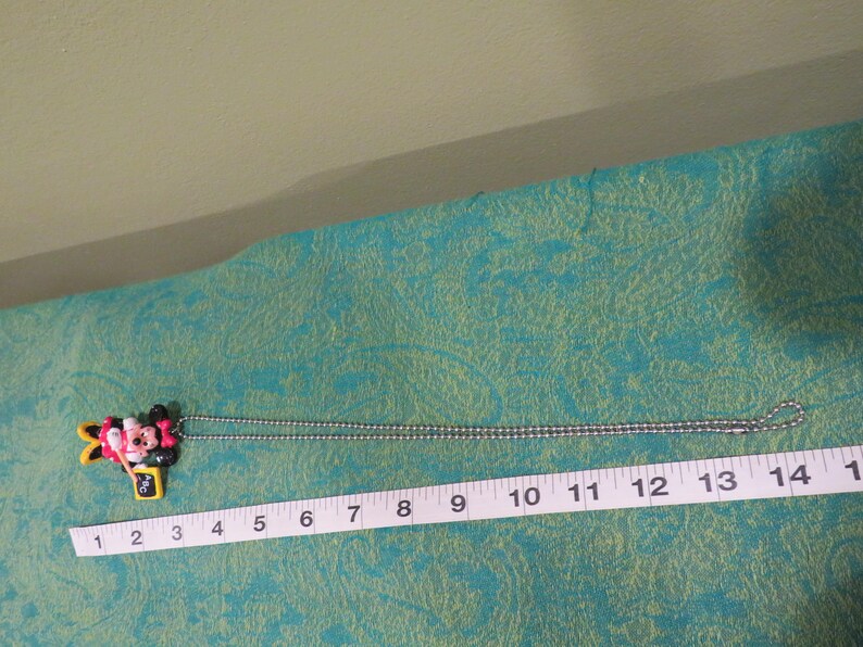 Peut inclure: Un collier avec pendentif Minnie Mouse et cha&icirc;ne argent&eacute;e. Le pendentif est color&eacute;, repr&eacute;sentant le visage et le n&oelig;ud de Minnie. Le collier mesure environ 35,5 cm de long.