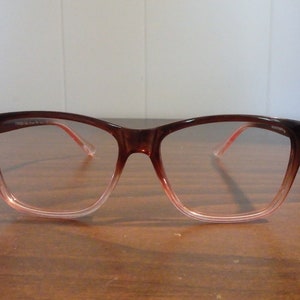May include: Brown plastic framed glasses with a gradient pink lens. The glasses have a square shape.