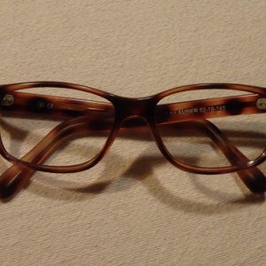 May include: Brown tortoise shell eyeglasses with a clear lens. The glasses have a metal hinge and the text "Alexander 52-18-147" is printed on the right temple.