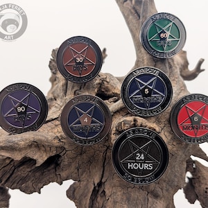 Könnte beinhalten: Eine Sammlung von sieben runden, dunklen Metallpins mit einem Pentagramm-Design. Jeder Pin zeigt den Text "AS ABOVE SO BELOW" und einen anderen Zeitrahmen, wie "30 TAGE" oder "24 STUNDEN", in verschiedenen Farben.