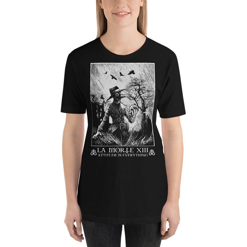 May include: Black and white graphic t-shirt featuring a plague doctor holding a skull. The text "#LA MORTE XIII" and "ATTITUDE IS EVERYTHING" is printed below the image.