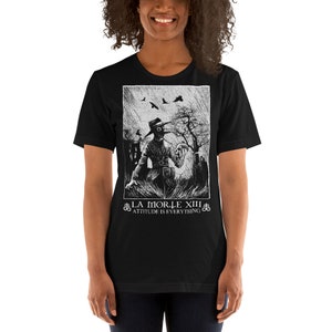 May include: Black t-shirt with a white graphic print of a person wearing a plague doctor mask and holding a skull. The text "LA MORTE XIII" and "ATTITUDE IS EVERYTHING" is printed below the graphic.