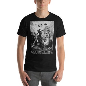 May include: Black t-shirt with a white graphic print of a person wearing a plague doctor mask and holding a skull. The text "LA MORTE XIII" and "ATTITUDE IS EVERYTHING" is printed below the graphic.