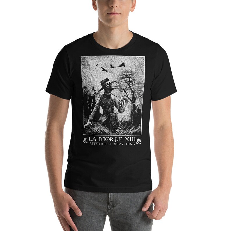 May include: Black t-shirt with a white graphic print of a person wearing a plague doctor mask and holding a skull. The text "LA MORTE XIII" and "ATTITUDE IS EVERYTHING" is printed below the graphic.