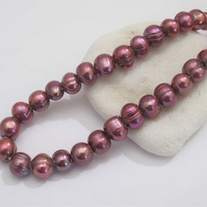 Peut inclure: Un brin de perles d'eau douce de couleur violet foncé. Les perles sont rondes et ont une finition lisse et irisée.