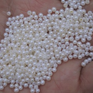 May include: A large pile of white pearl beads. The beads are round and have a smooth, glossy finish.