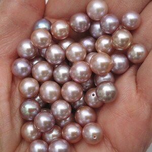 May include: A pile of iridescent pink and purple pearls in a hand. The pearls are round and smooth.