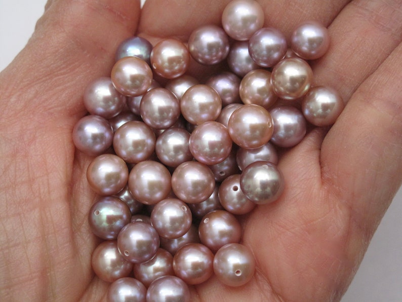 May include: A pile of iridescent pink and purple pearls in a hand. The pearls are round and smooth.