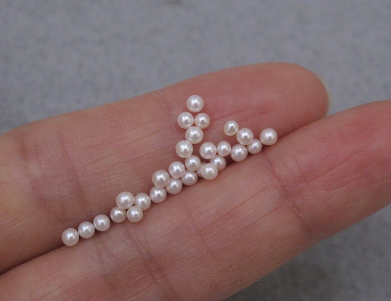 May include: A collection of white round pearls, scattered on a hand.