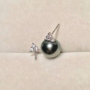 May include: A pair of earrings featuring a single black pearl with a silver setting and a small silver triangle with three clear stones.