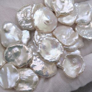 May include: A collection of white, iridescent, irregularly shaped freshwater pearls. The pearls are smooth and have a natural, organic look.