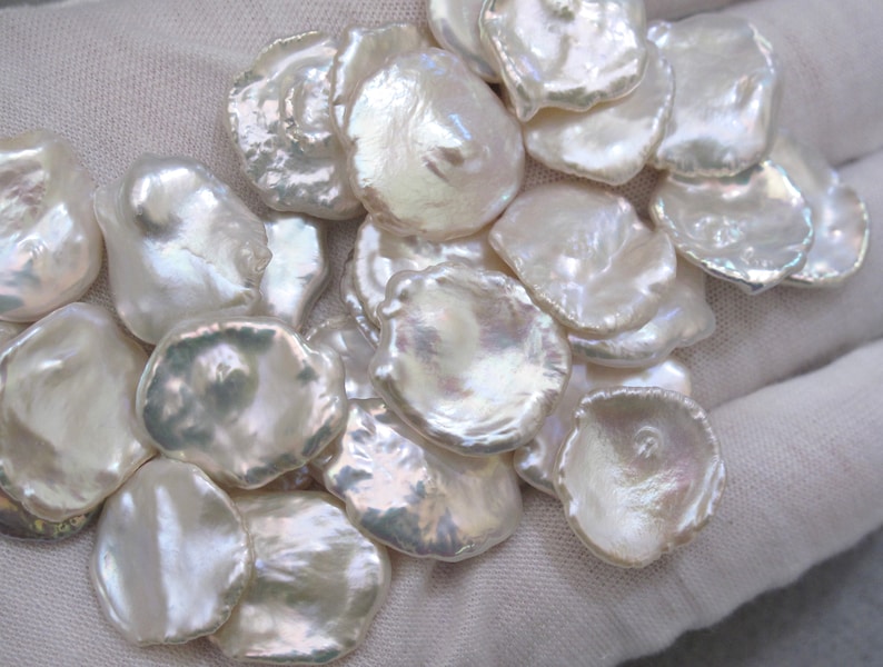 May include: A collection of white, iridescent, irregularly shaped freshwater pearls. The pearls are smooth and have a natural, organic look.