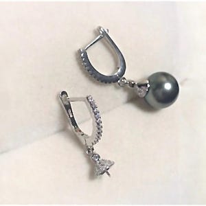 May include: A pair of silver hoop earrings with a small pearl pendant hanging from each hoop. The hoops are decorated with small clear stones.