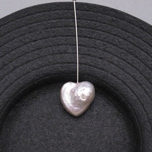 May include: A white heart-shaped pearl pendant hanging from a silver chain on a black background.