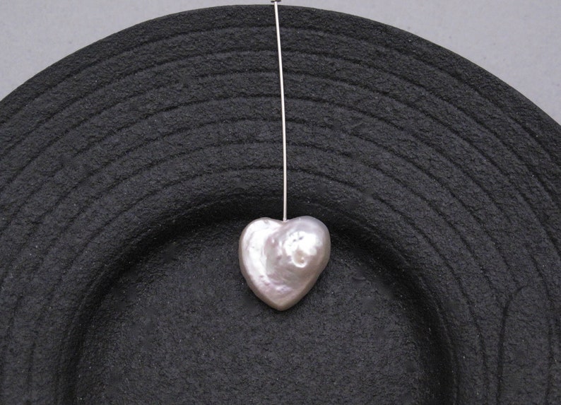 May include: A white heart-shaped pearl pendant hanging from a silver chain on a black background.