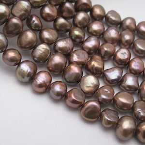 May include: A strand of brown freshwater pearls with an iridescent sheen. The pearls are irregularly shaped and have a smooth, polished surface.