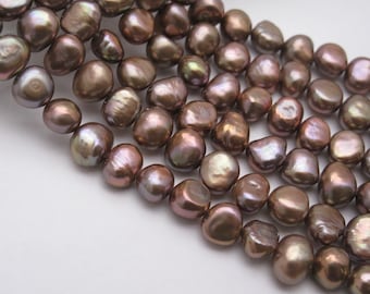 May include: A strand of brown freshwater pearls with an iridescent sheen. The pearls are irregularly shaped and have a smooth, polished surface.
