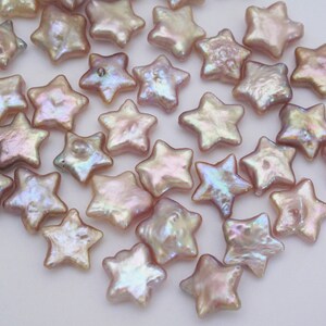 May include: A collection of iridescent pink star-shaped pearl beads. The beads are scattered on a white surface.