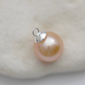 May include: A single, pale pink pearl with a silver cap and loop for hanging. The pearl is smooth and round, and the cap is shiny.