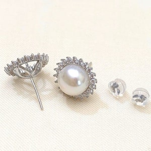 May include: A pair of silver earrings with a pearl and clear stones. The earrings are shown with two clear plastic earring backs.